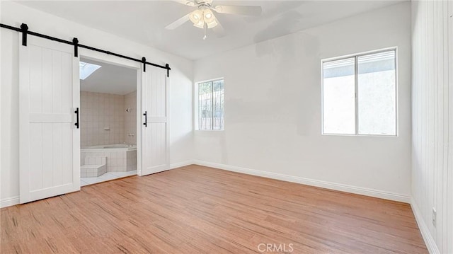 unfurnished room featuring a barn door, light wood-style flooring, baseboards, and ceiling fan