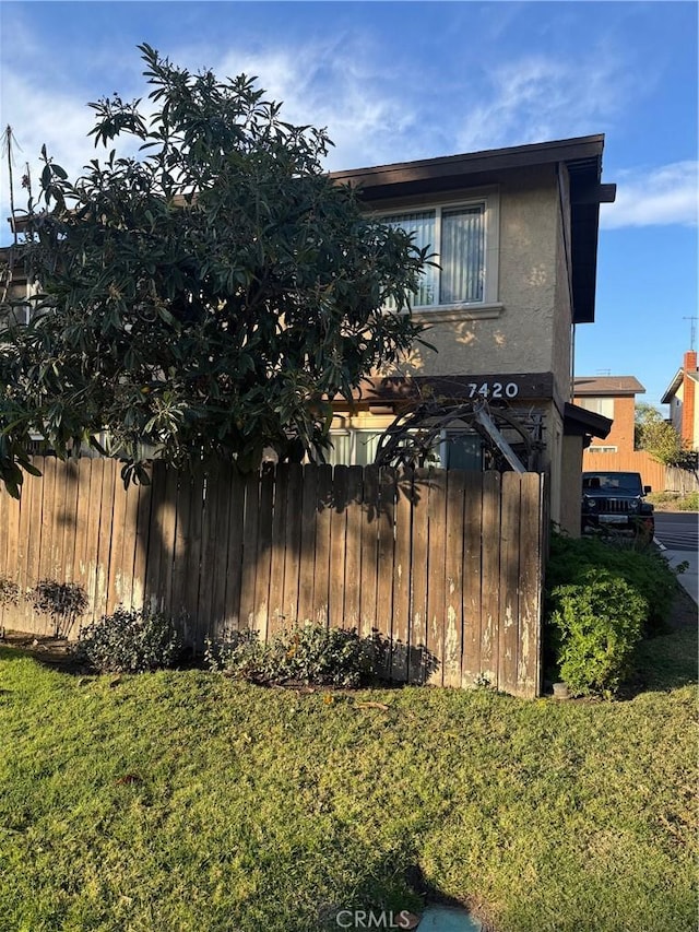 view of side of property with fence, a lawn, and stucco siding