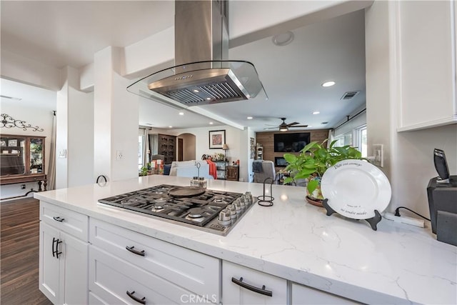 kitchen featuring light stone counters, open floor plan, arched walkways, stainless steel gas stovetop, and island range hood