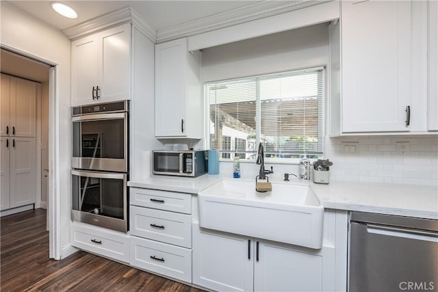 kitchen with a sink, stainless steel appliances, dark wood-type flooring, white cabinetry, and backsplash