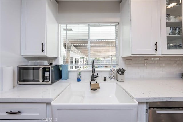 kitchen featuring a sink, stainless steel microwave, glass insert cabinets, and white cabinets