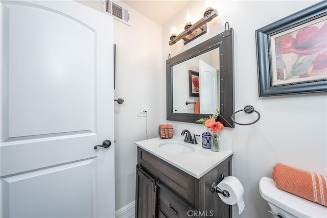 half bath with vanity, toilet, and visible vents