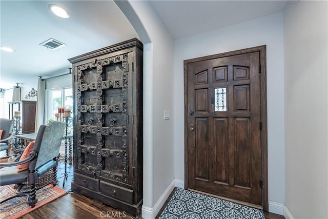 foyer with arched walkways, visible vents, baseboards, and wood finished floors