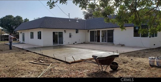 back of house featuring mansard roof, a patio, and stucco siding