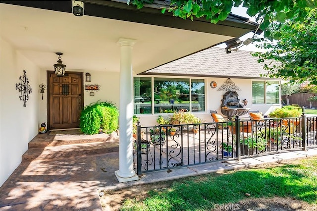 doorway to property featuring stucco siding, a shingled roof, and fence