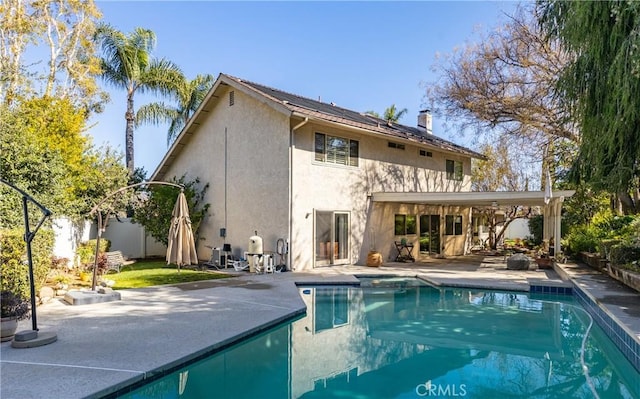 rear view of house with solar panels, an outdoor pool, a patio, and stucco siding