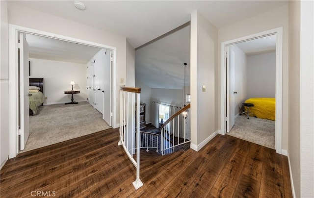 hallway featuring baseboards, an upstairs landing, dark wood finished floors, and dark carpet