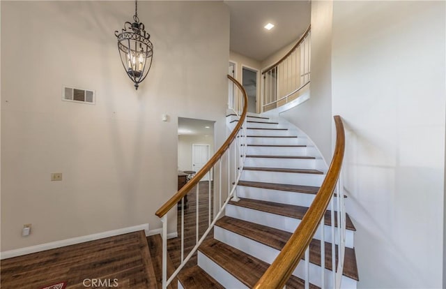 stairs with visible vents, baseboards, an inviting chandelier, wood finished floors, and a towering ceiling