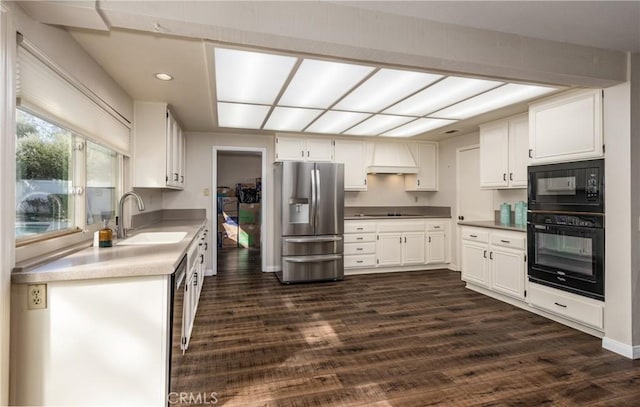 kitchen with black appliances, dark wood-type flooring, custom range hood, white cabinetry, and a sink