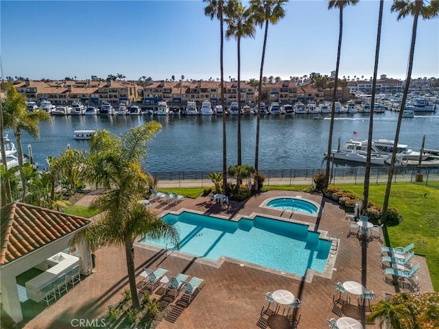 pool featuring a community hot tub, a water view, a lawn, a patio area, and a residential view