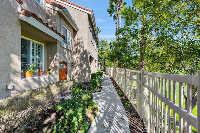 view of side of home featuring a tiled roof, fence, and stucco siding