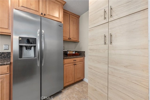 kitchen featuring dark stone counters, light tile patterned flooring, stainless steel fridge, and a textured ceiling