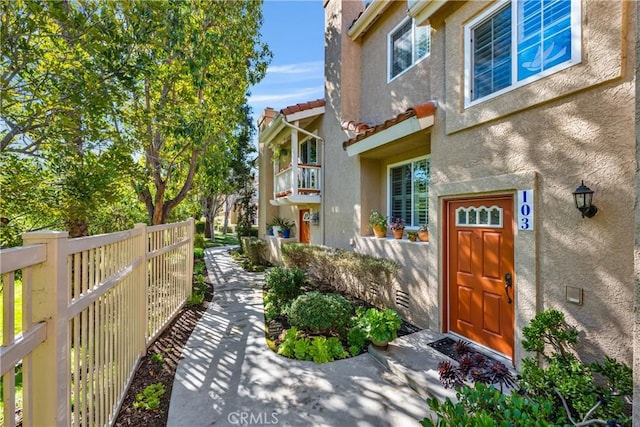 doorway to property featuring a tiled roof, fence, and stucco siding