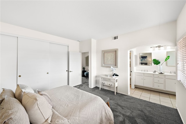 bedroom featuring visible vents, ensuite bathroom, a closet, arched walkways, and light colored carpet