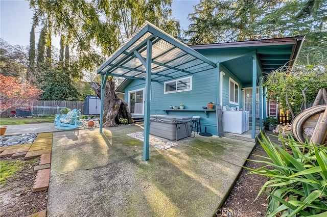 rear view of house featuring a hot tub, fence, a shed, a patio area, and an outbuilding