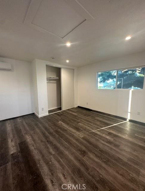 unfurnished bedroom featuring dark wood finished floors, a closet, and a wall unit AC