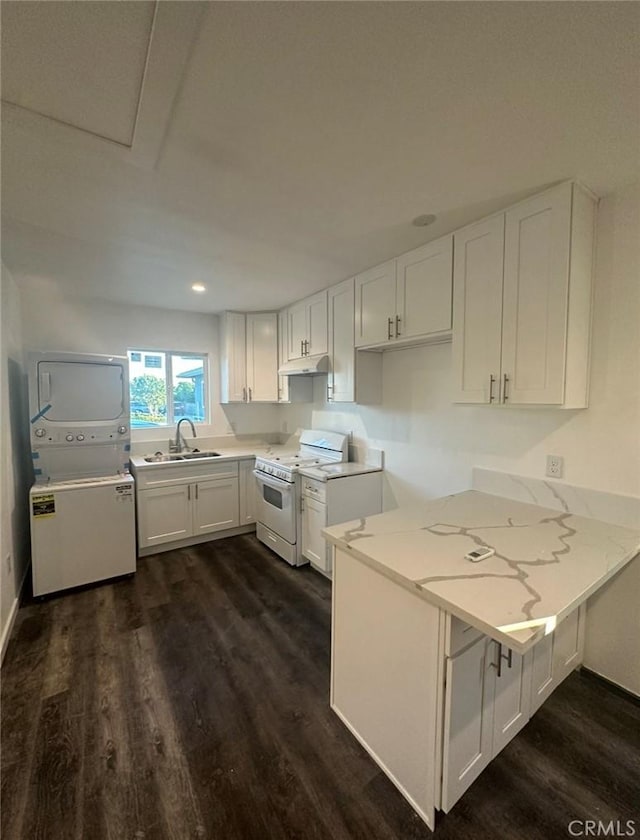 kitchen with a peninsula, white gas stove, dark wood-type flooring, stacked washer / drying machine, and white cabinetry