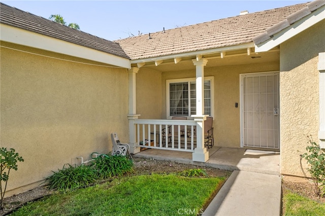 entrance to property with a tile roof, covered porch, and stucco siding