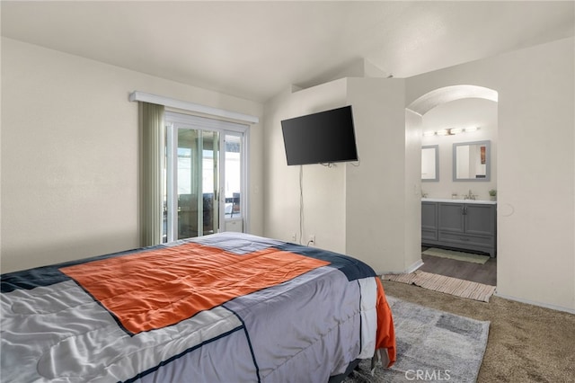 carpeted bedroom featuring baseboards, arched walkways, a sink, vaulted ceiling, and ensuite bathroom