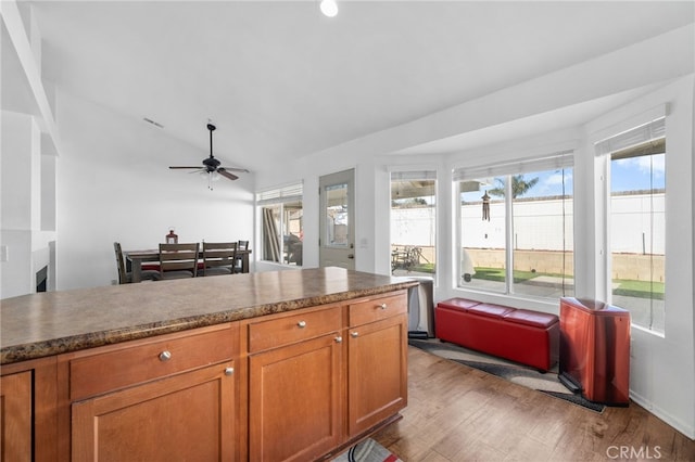 kitchen featuring brown cabinets, dark countertops, wood finished floors, ceiling fan, and vaulted ceiling