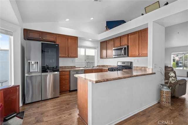 kitchen with lofted ceiling, brown cabinets, appliances with stainless steel finishes, dark wood-style floors, and a sink