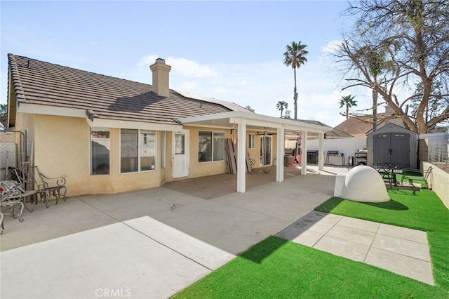 rear view of property with a storage unit, fence, an outdoor structure, and stucco siding