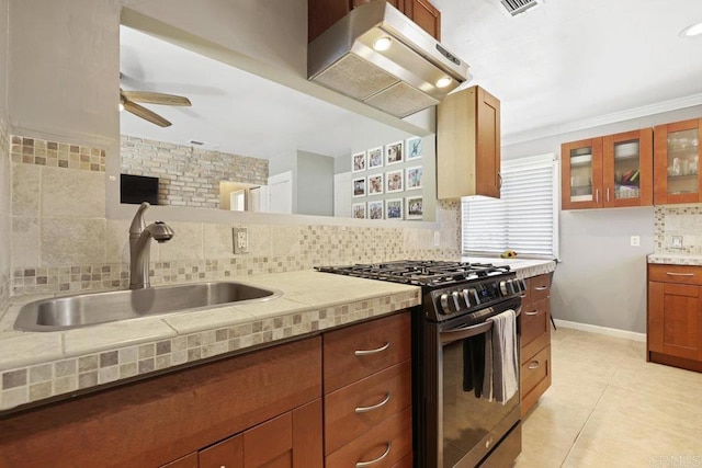 kitchen with tasteful backsplash, glass insert cabinets, under cabinet range hood, gas stove, and a sink