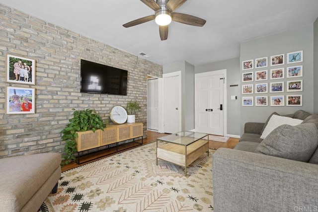 living room featuring visible vents, brick wall, ceiling fan, baseboards, and wood finished floors