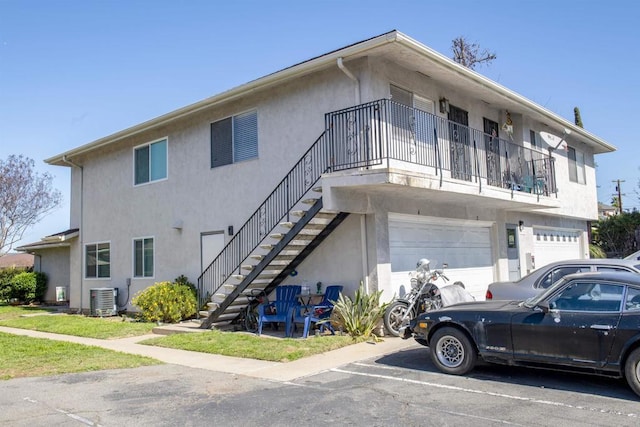 rear view of property with stucco siding, an attached garage, stairs, and central AC