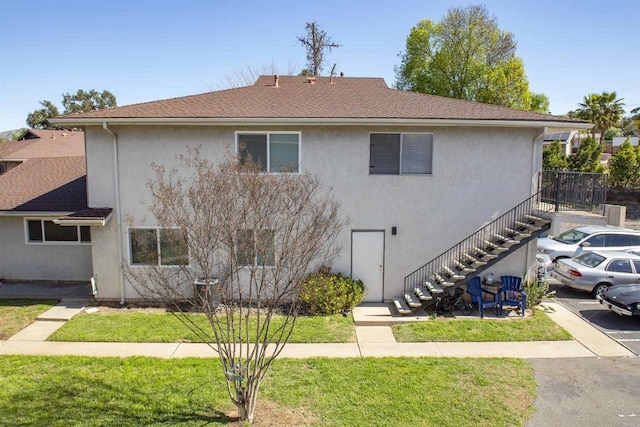 view of front facade featuring stairway, stucco siding, a front lawn, and roof with shingles