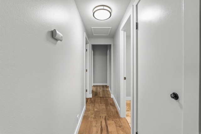 corridor featuring baseboards, attic access, and light wood-style flooring