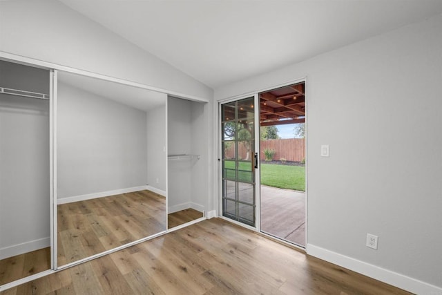 unfurnished bedroom with access to exterior, wood finished floors, baseboards, and lofted ceiling