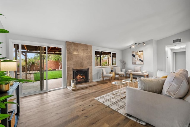 living room with a tiled fireplace, lofted ceiling, wood finished floors, and visible vents