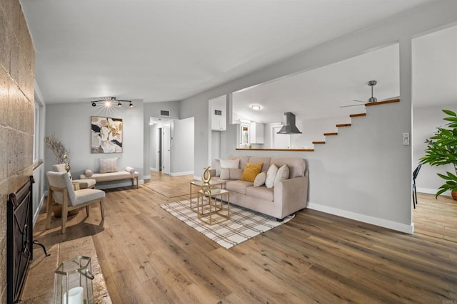 living area with light wood-type flooring, baseboards, a fireplace, lofted ceiling, and stairs