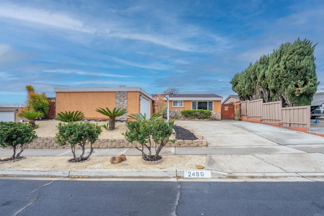 view of front of house with concrete driveway, an attached garage, fence, and stucco siding