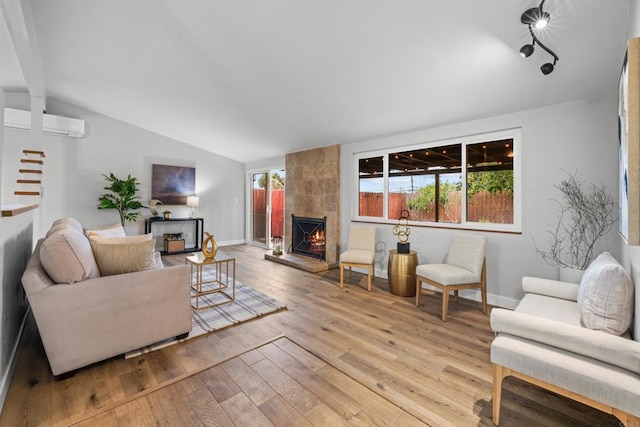 living room featuring a wall mounted air conditioner, lofted ceiling, wood finished floors, a fireplace, and baseboards