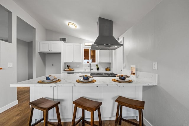 kitchen featuring visible vents, a peninsula, white cabinetry, and island range hood