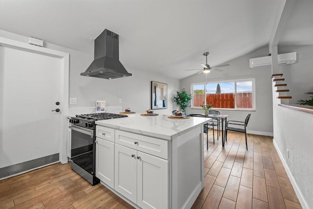 kitchen with light wood-style flooring, stainless steel range with gas stovetop, extractor fan, an AC wall unit, and white cabinetry