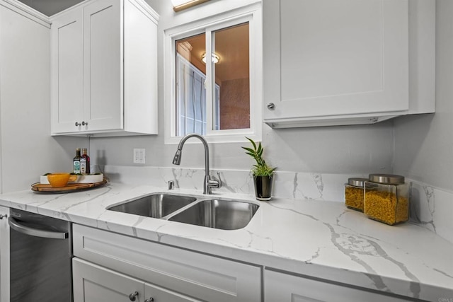 kitchen with light stone counters, white cabinetry, and a sink