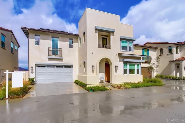 view of front of house with stucco siding, an attached garage, a balcony, and driveway