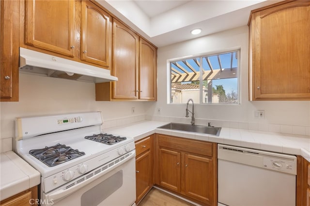 kitchen featuring white appliances, tile countertops, under cabinet range hood, and a sink