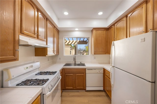 kitchen featuring light wood finished floors, tile counters, under cabinet range hood, white appliances, and a sink