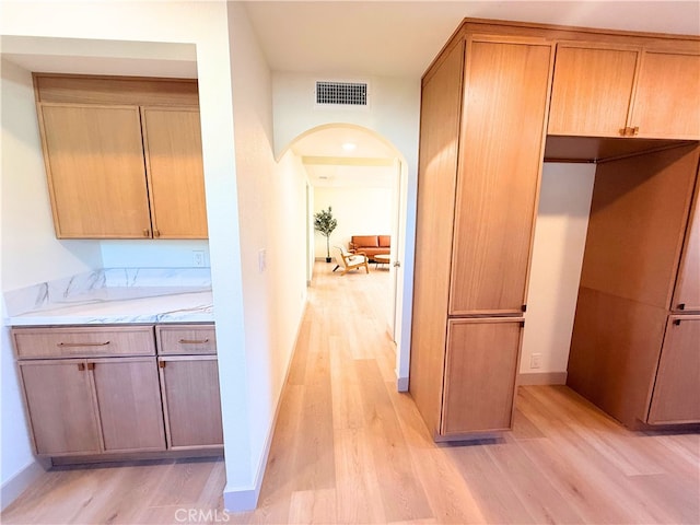 corridor featuring light wood-type flooring, visible vents, baseboards, and arched walkways