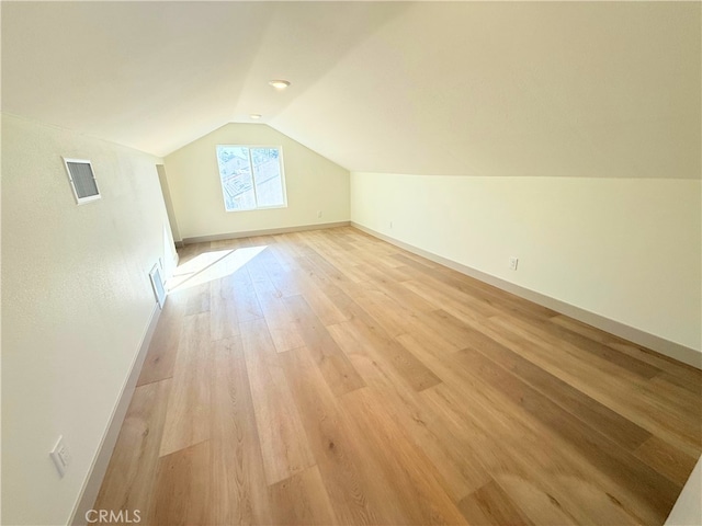 bonus room featuring light wood finished floors, visible vents, baseboards, and vaulted ceiling