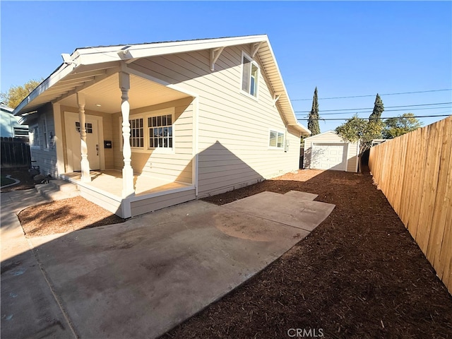 rear view of house featuring an outdoor structure, fence, a detached garage, and a patio area