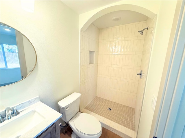 bathroom featuring a tile shower, vanity, and toilet