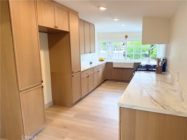 kitchen with light stone countertops, light wood finished floors, recessed lighting, light brown cabinetry, and a sink