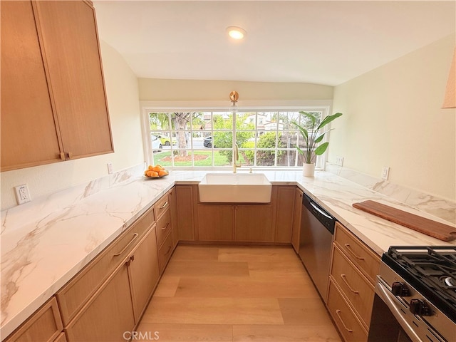 kitchen with light stone counters, light wood-style floors, stainless steel appliances, and a sink