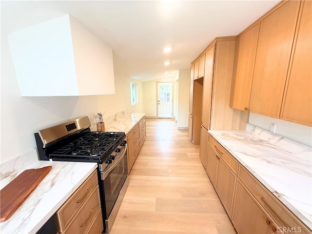 kitchen featuring stainless steel gas range oven, light stone counters, light brown cabinetry, and light wood finished floors