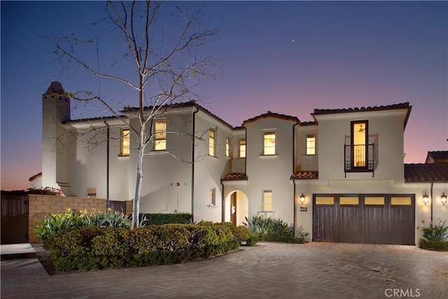 mediterranean / spanish-style home featuring a tiled roof, decorative driveway, a garage, and stucco siding